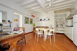 A dining area with a wooden table and chairs, a ceiling fan, and a kitchen area with white cabinets and a stone backsplash.