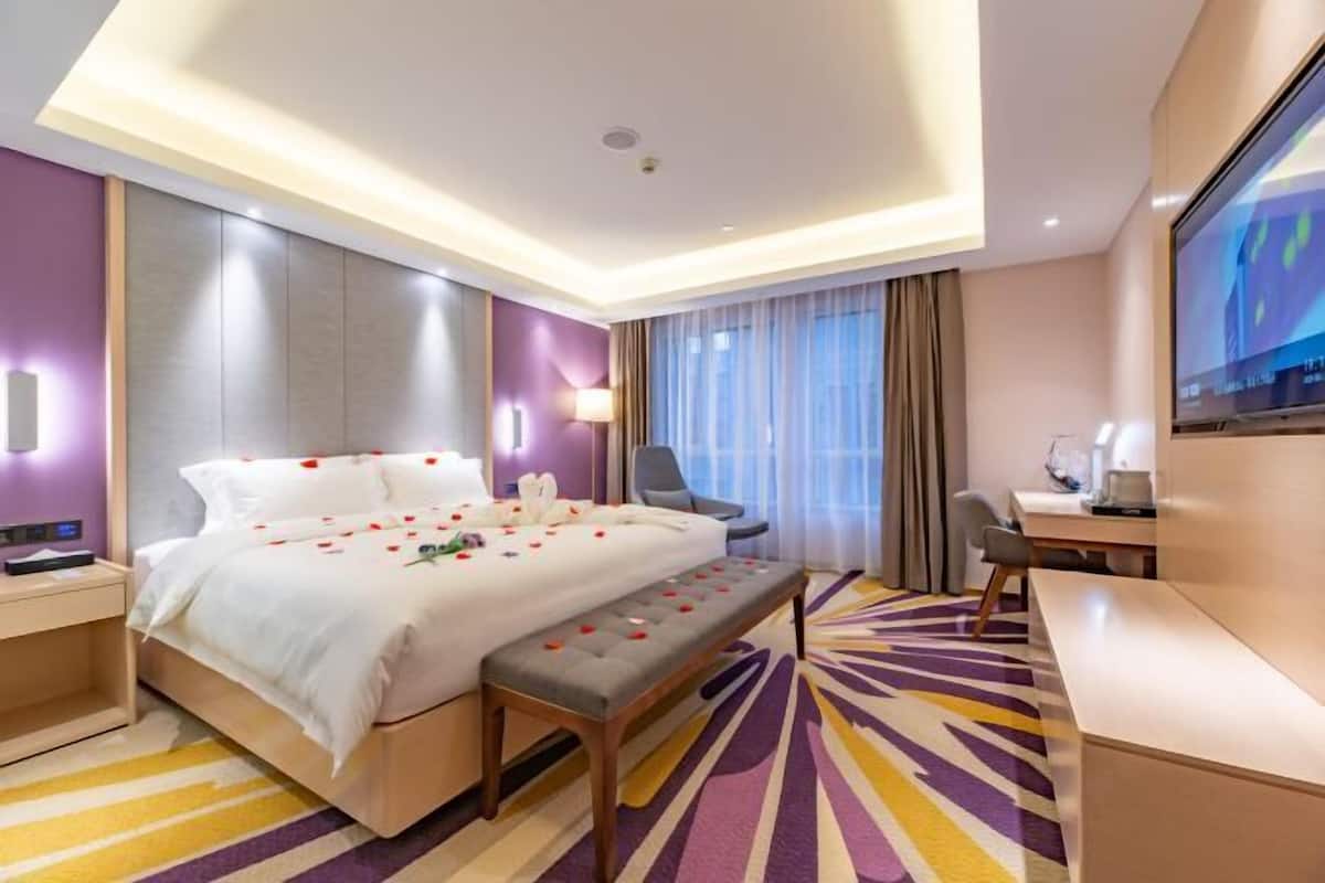 A modern hotel room with a large bed, a desk, a chair, and a TV.
