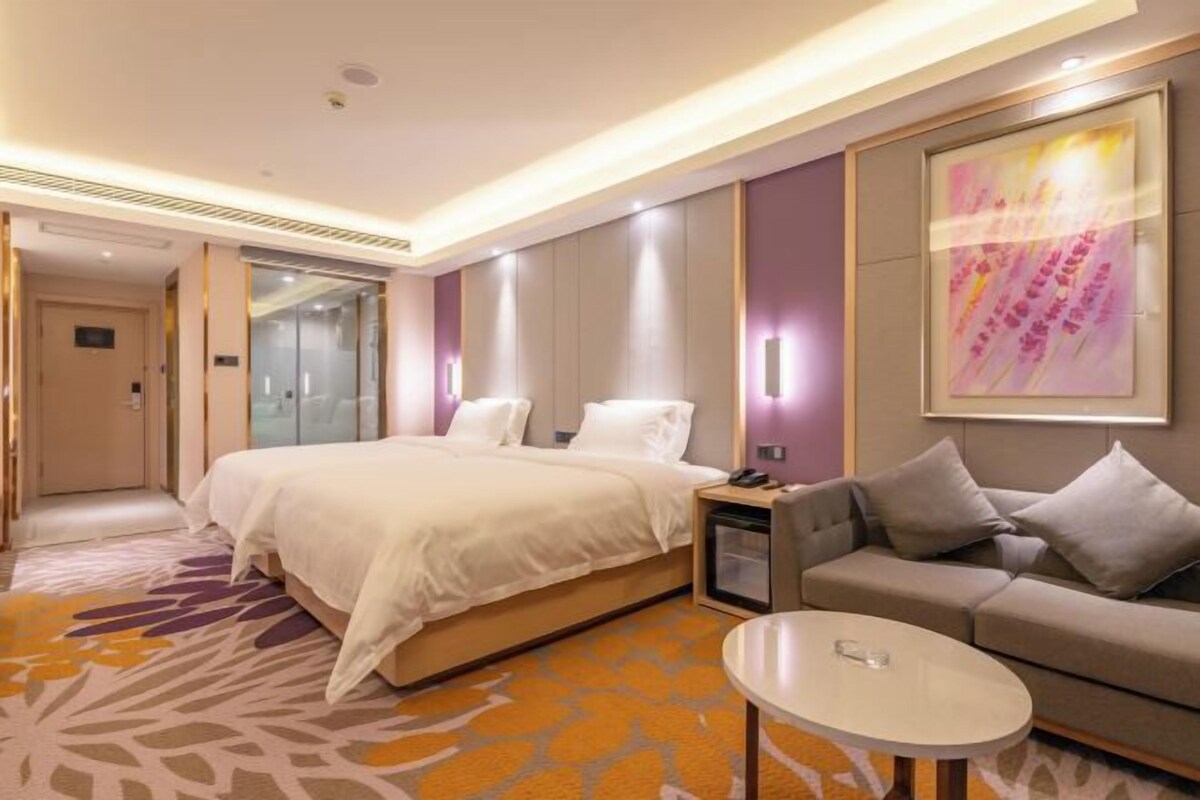 A hotel room with a large bed, a sofa, a small table, and a painting on the wall.
