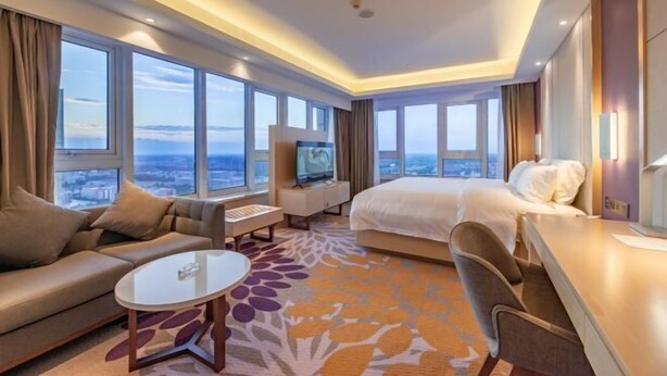 A hotel room with a large bed, a sofa, a desk, a TV, and a view of the city. - Lavande Hotel (Heze Daxue Road Branch) (Heze)