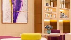 A modern hotel lobby with a large abstract painting, a glass display case with souvenirs, and a round table with a vase of flowers. - Lavande Hotel (Heze Daxue Road Branch) (Heze)