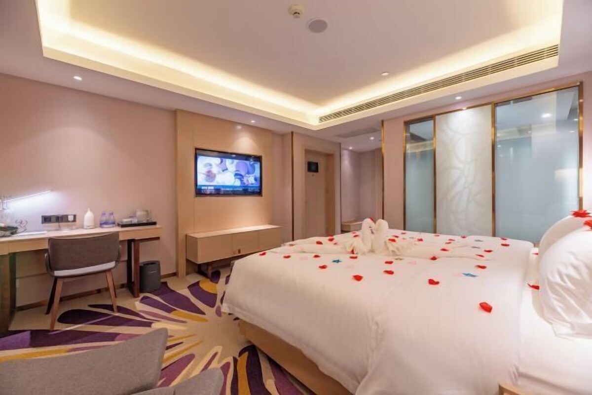 Una habitación de hotel con cama, escritorio, televisor y un ventanal grande.