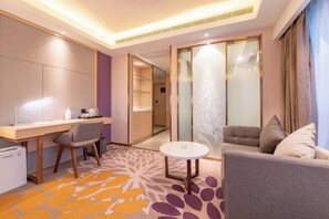 A hotel room with a desk, two chairs, a sofa, a small round table, and a patterned carpet. - Lavande Hotel (Heze Daxue Road Branch) (Heze)