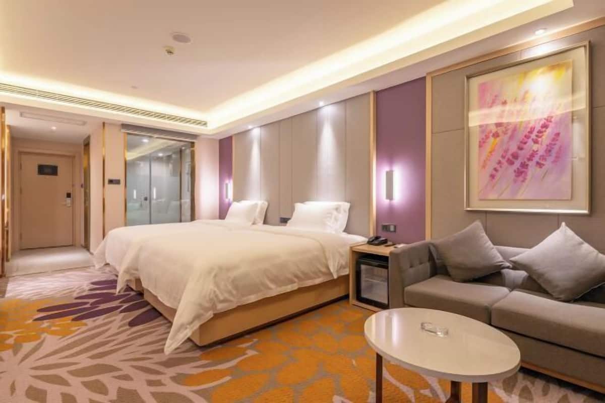 A hotel room with a bed, a sofa, a small table, a nightstand, and a large abstract painting on the wall.