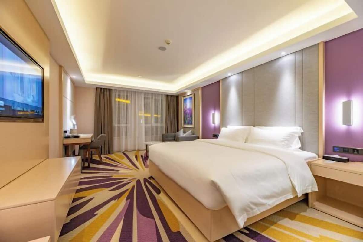 A modern hotel room with a large bed, a desk, and a TV.