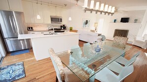 Una cocina moderna con electrodomésticos de acero inoxidable, una mesa de comedor de vidrio y armarios de colores claros.