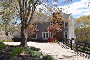Une maison à deux étages avec une allée en gravier, une clôture en bois et une chaise rouge devant.