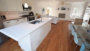 Una cocina moderna con armarios blancos, una isla grande y un comedor con mesa de vidrio.