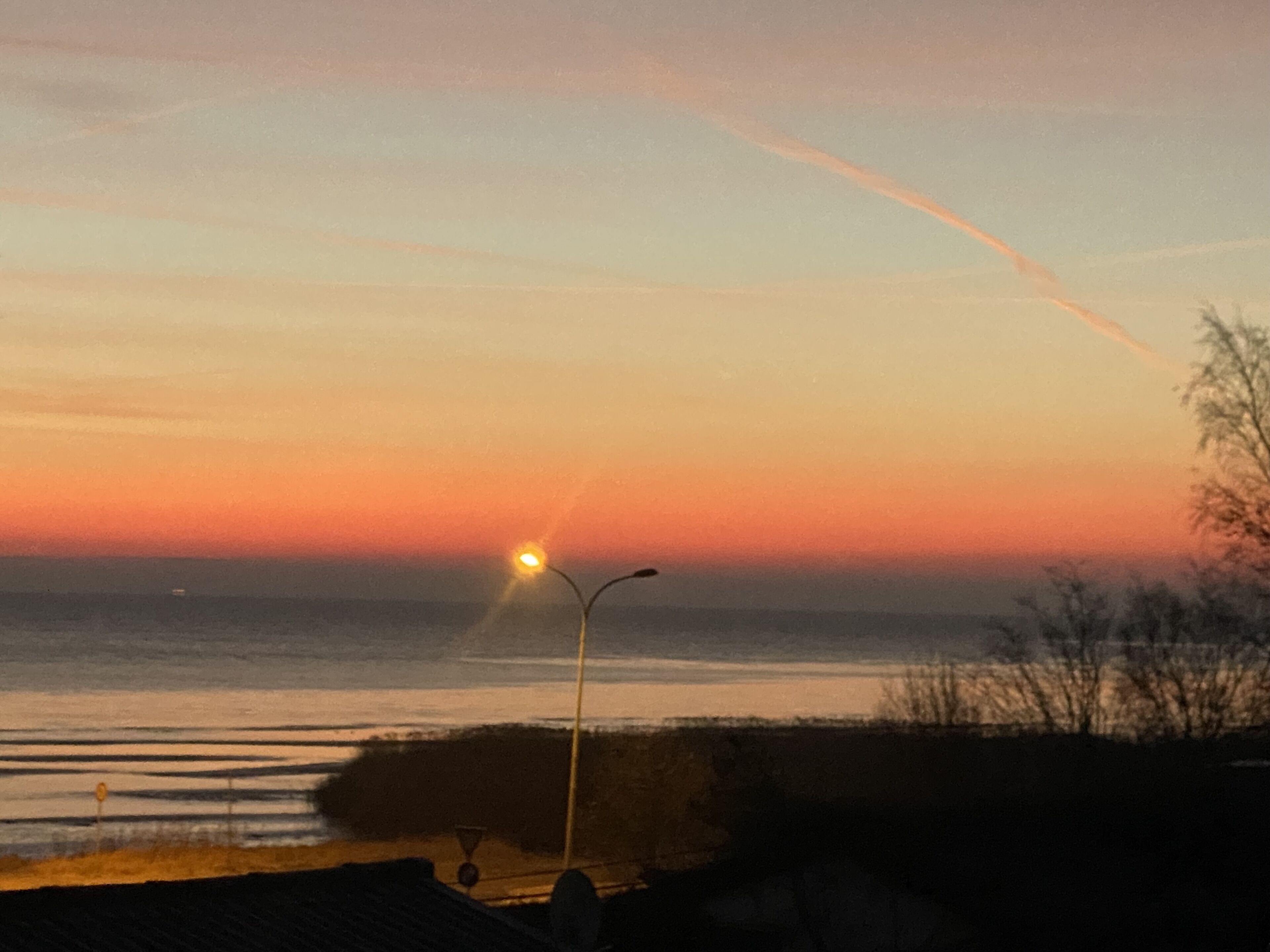 Ein Sonnenuntergang über einem Gewässer, mit einer Straßenlaterne und weiter Ferne.