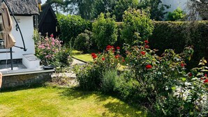 A garden with a thatched-roof house, a white house, and a hedge. - Thatched-roof holiday home with water view, garden and fireplace  (Stahlbrode)