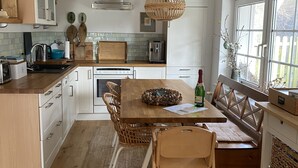 A modern kitchen with white cabinets, a wooden dining table, and a built-in bench. - Thatched-roof holiday home with water view, garden and fireplace  (Stahlbrode)