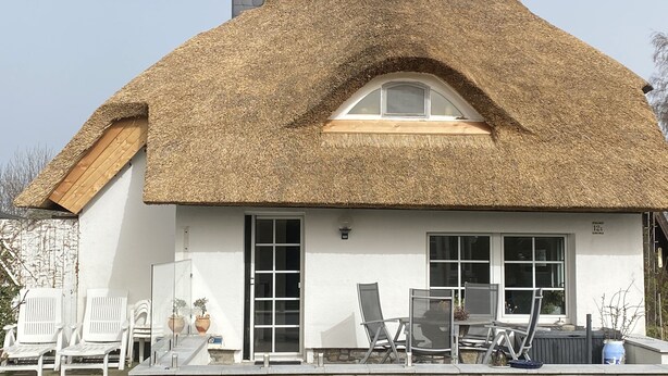 A house with a thatched roof, white exterior walls, and a stone foundation. There are white chairs and a table outside, and a ladder is leaning against the house. - Thatched-roof holiday home with water view, garden and fireplace  (Stahlbrode)