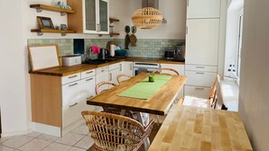 A modern kitchen with wooden cabinets, a dining table with wicker chairs, and a hanging light fixture. - Thatched-roof holiday home with water view, garden and fireplace  (Stahlbrode)