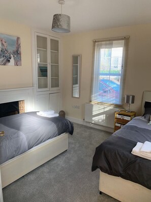 Ein Schlafzimmer mit zwei Betten, einem Kleiderschrank, einem Heizkörper und einem Fenster mit Jalousien.