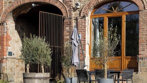 Un espace extérieur aménagé avec des sièges, un bâtiment en briques, une porte en bois et des plantes en pot.