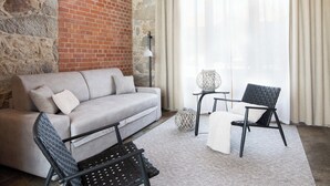 Un salon avec un mur en briques, un canapé, un fauteuil, une lampe et une grande fenêtre avec des rideaux.