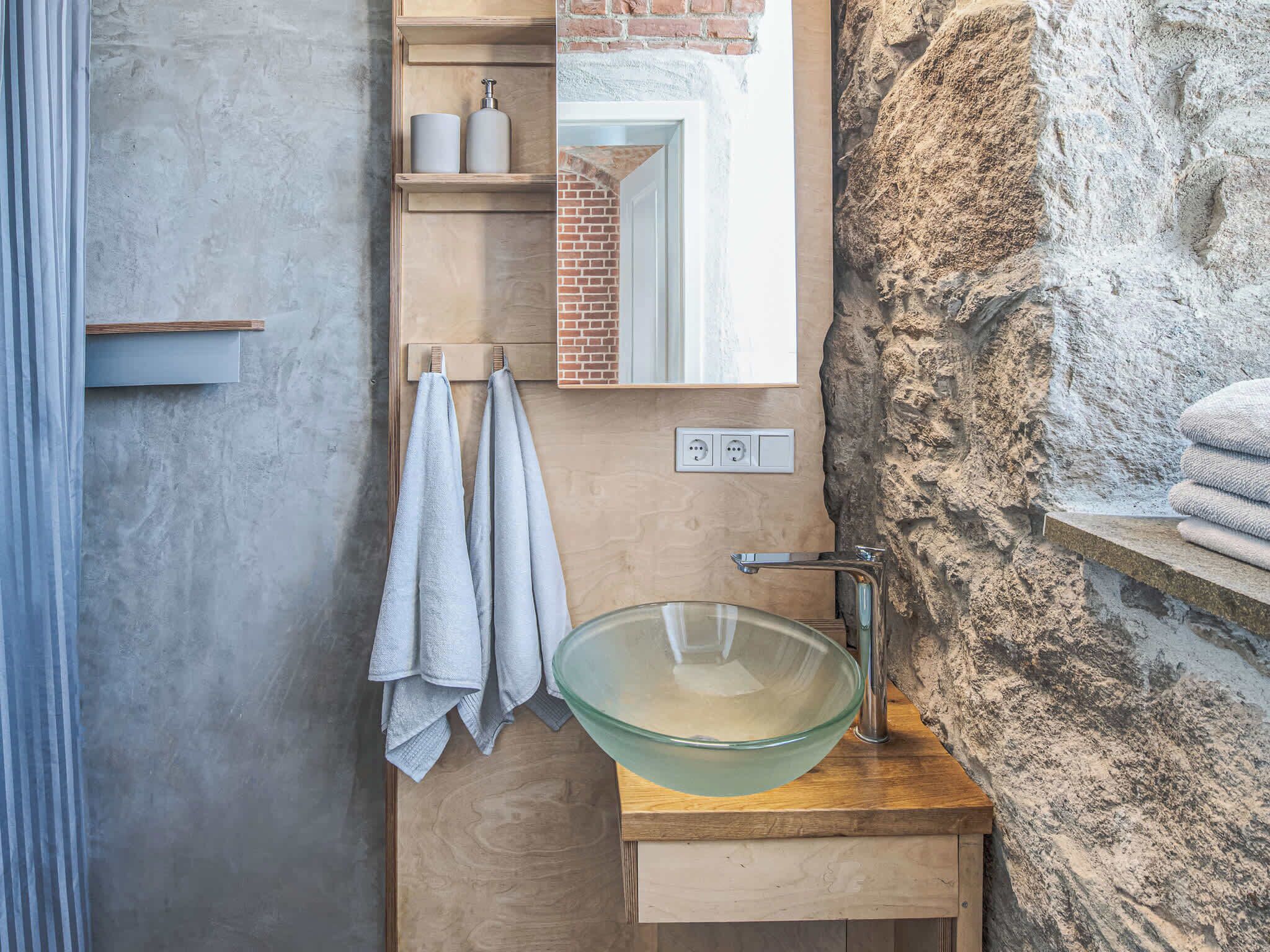 A bathroom with a glass bowl sink, wooden vanity, towels, a mirror, and a stone wall.