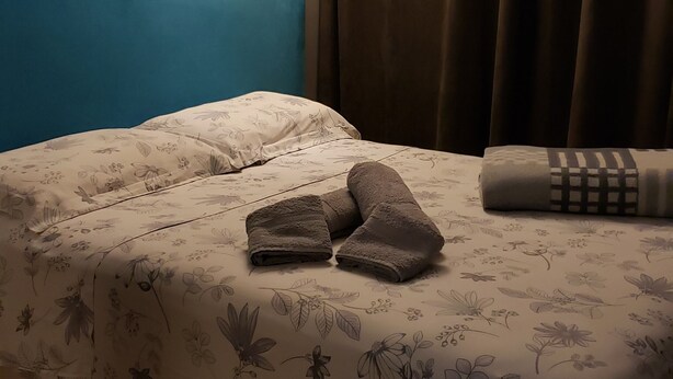 A bed with floral bedding, a blue headboard, and two towels. - Apto. Completo Prox a av. Paulista (São Paulo)