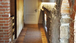 Een smalle gang met houten vloer, een bakstenen muur en een deur aan het einde.