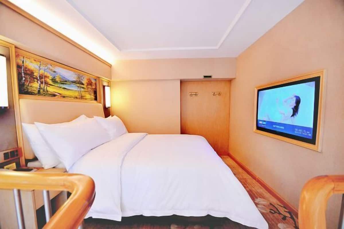 A hotel room with a bed, a television, a painting, and a wooden door.