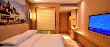 A hotel room with a bed, a television, a painting on the wall, and a door leading to another room.