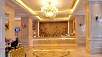 A hotel lobby with a reception desk, a chandelier, and a large decorative wall.