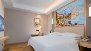 Une chambre d’hôtel avec un grand lit, une table de chevet avec une lampe, un tableau au mur et un plancher en bois.