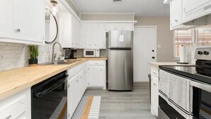 Une cuisine moderne avec des meubles blancs, des appareils en acier inoxydable, un plan de travail en bois et un tapis à motifs.