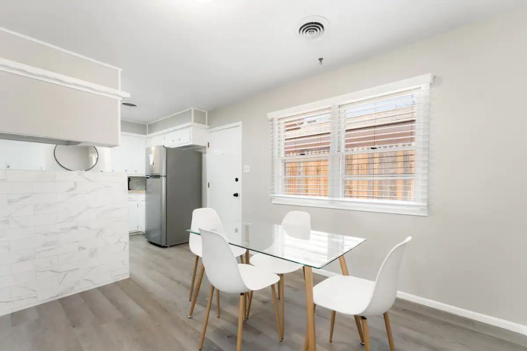 A modern kitchen with white cabinetry, a glass dining table, and white chairs.