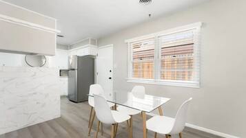 A modern kitchen with white cabinetry, a glass dining table, and white chairs.