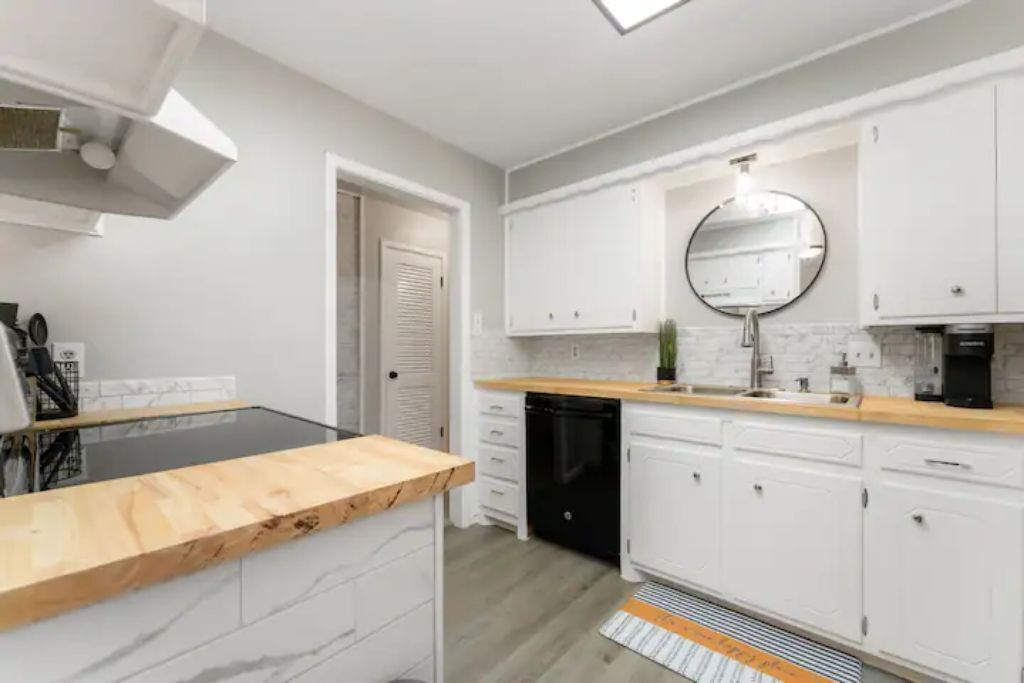 A modern kitchen with white cabinets, a black dishwasher, and a wooden countertop.