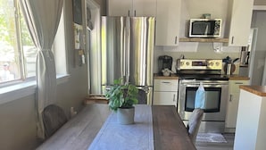 Una cucina moderna con frigorifero, microonde e forno in acciaio inossidabile. È presente un tavolo da pranzo con un vaso di piante e una sedia.