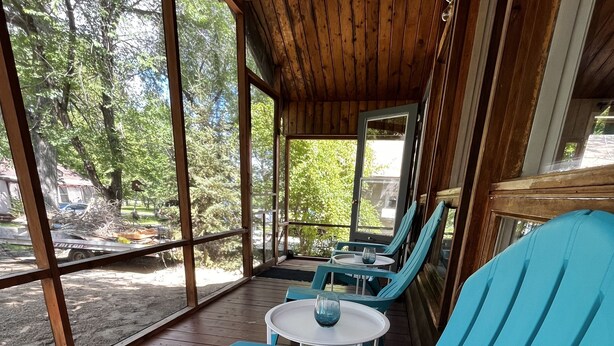 Un'area salotto esterna coperta con sedie blu e un tavolino, ampie finestre e un soffitto in legno.