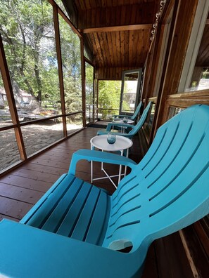 Un espacio al aire libre cubierto con sillas azules, una mesa pequeña, ventanas grandes y techo de madera.