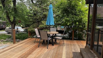 Relax on the outdoor deck surrounded by lush greenery and trees, with a table and chairs under a pergola.
