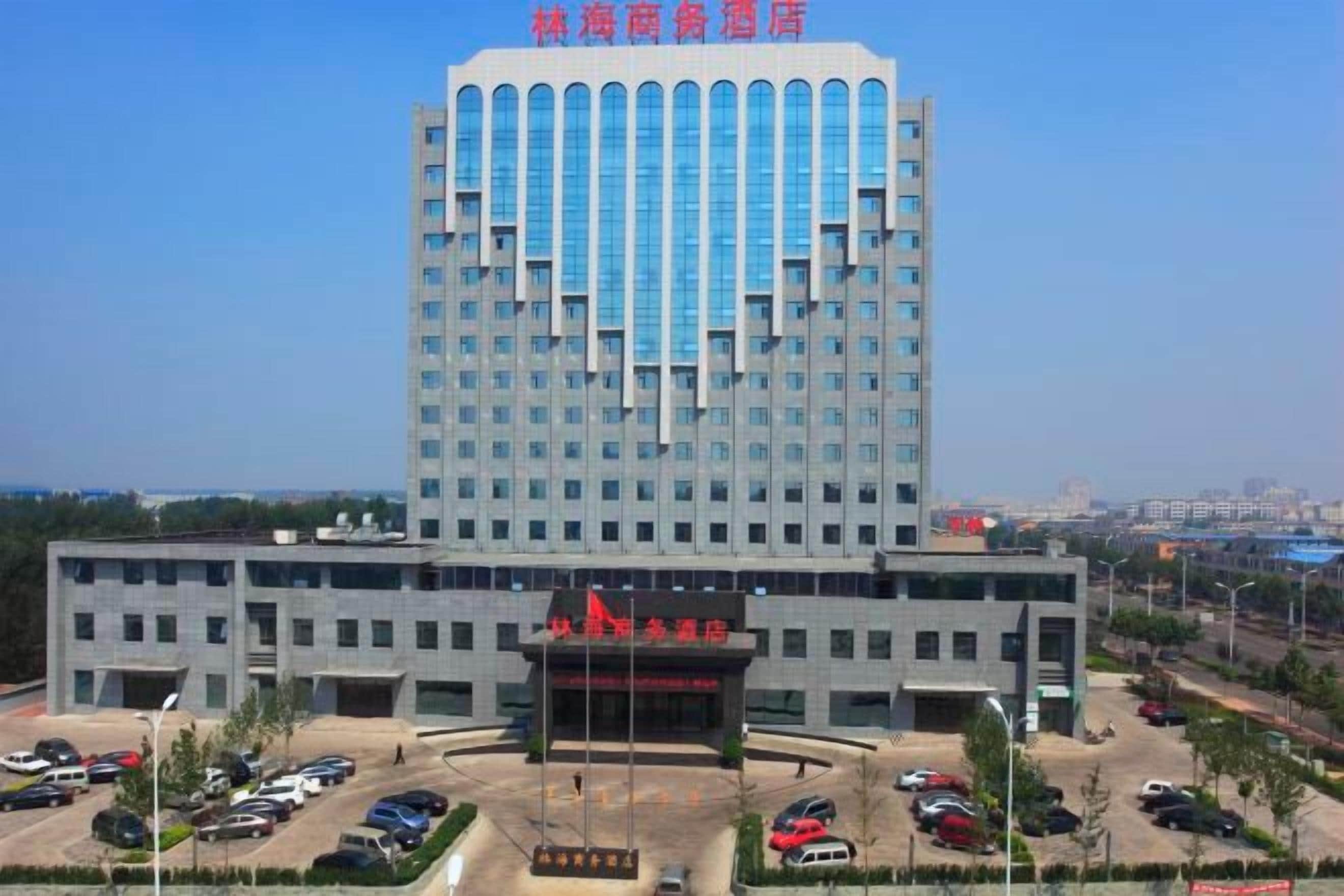 A multi-story hotel with a central entrance, parking area, and a view of the surrounding cityscape.
