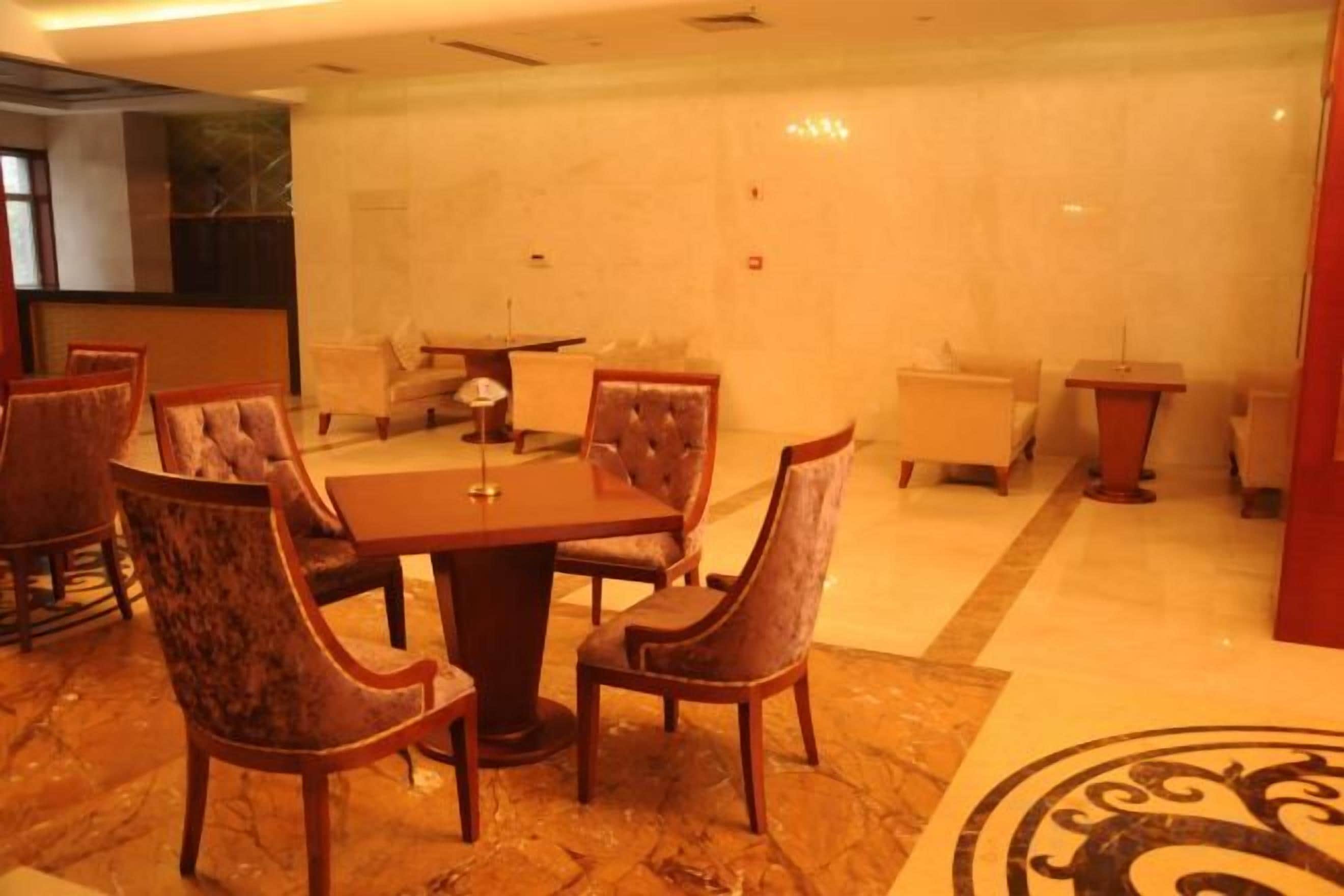 A hotel dining area with a rectangular table surrounded by upholstered chairs, a small round table, and a sofa.
