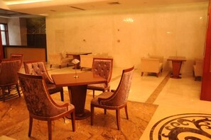 Un comedor de hotel con una mesa rectangular rodeada de sillones tapizados, una mesita redonda y un sofá.