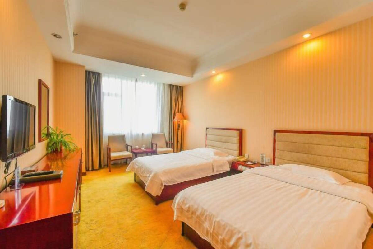 Une chambre d’hôtel avec deux lits, un bureau avec une télévision, une chaise et une fenêtre avec des rideaux.