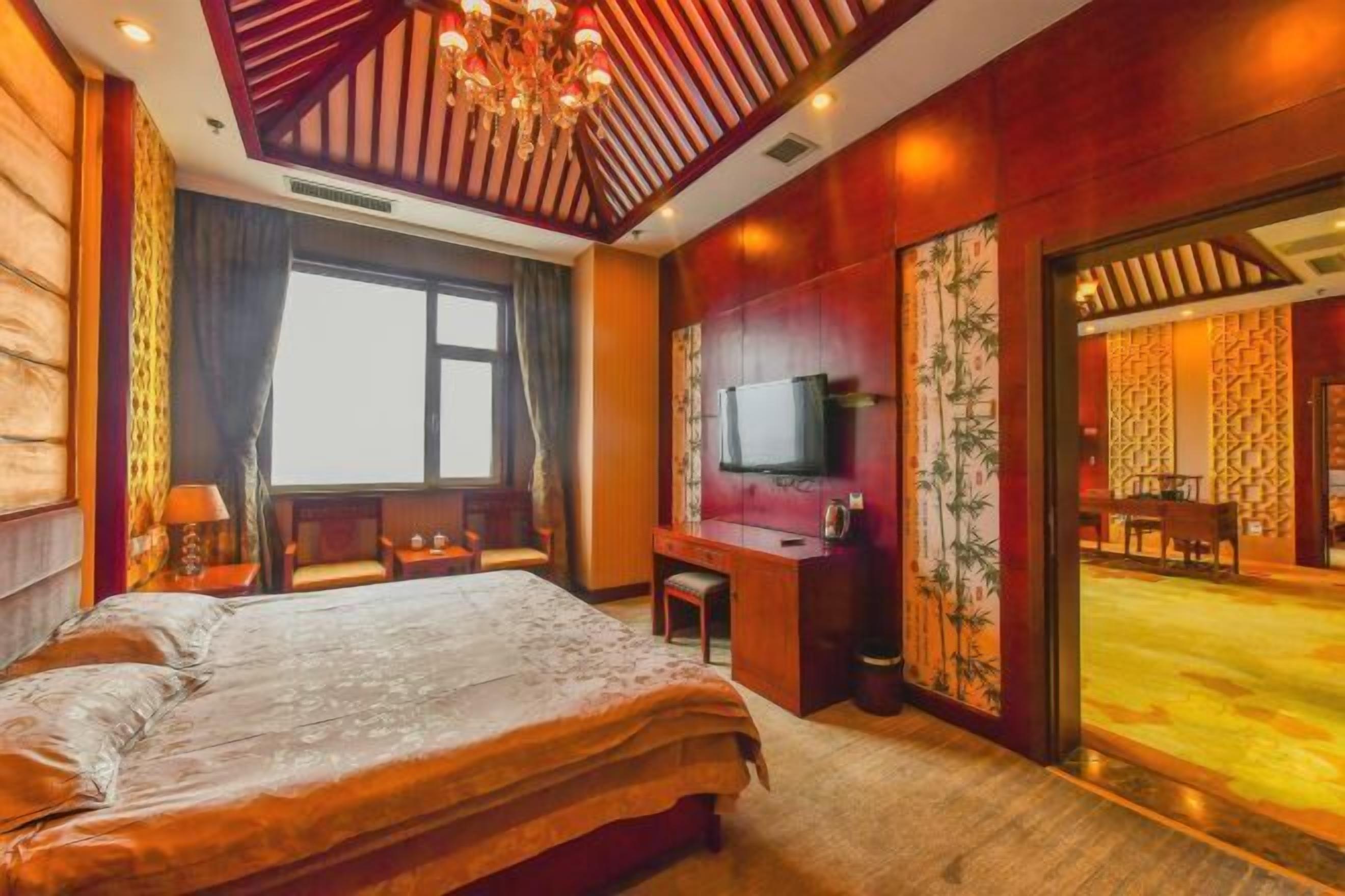A hotel room with a large bed, a desk, a television, and a view of a dining area.