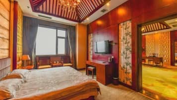 Habitación de hotel con una cama grande, un escritorio, televisor y vista a un comedor.