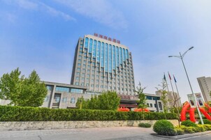 Un hotel de varios pisos con fachada moderna, un jardín bien cuidado y cielo despejado.