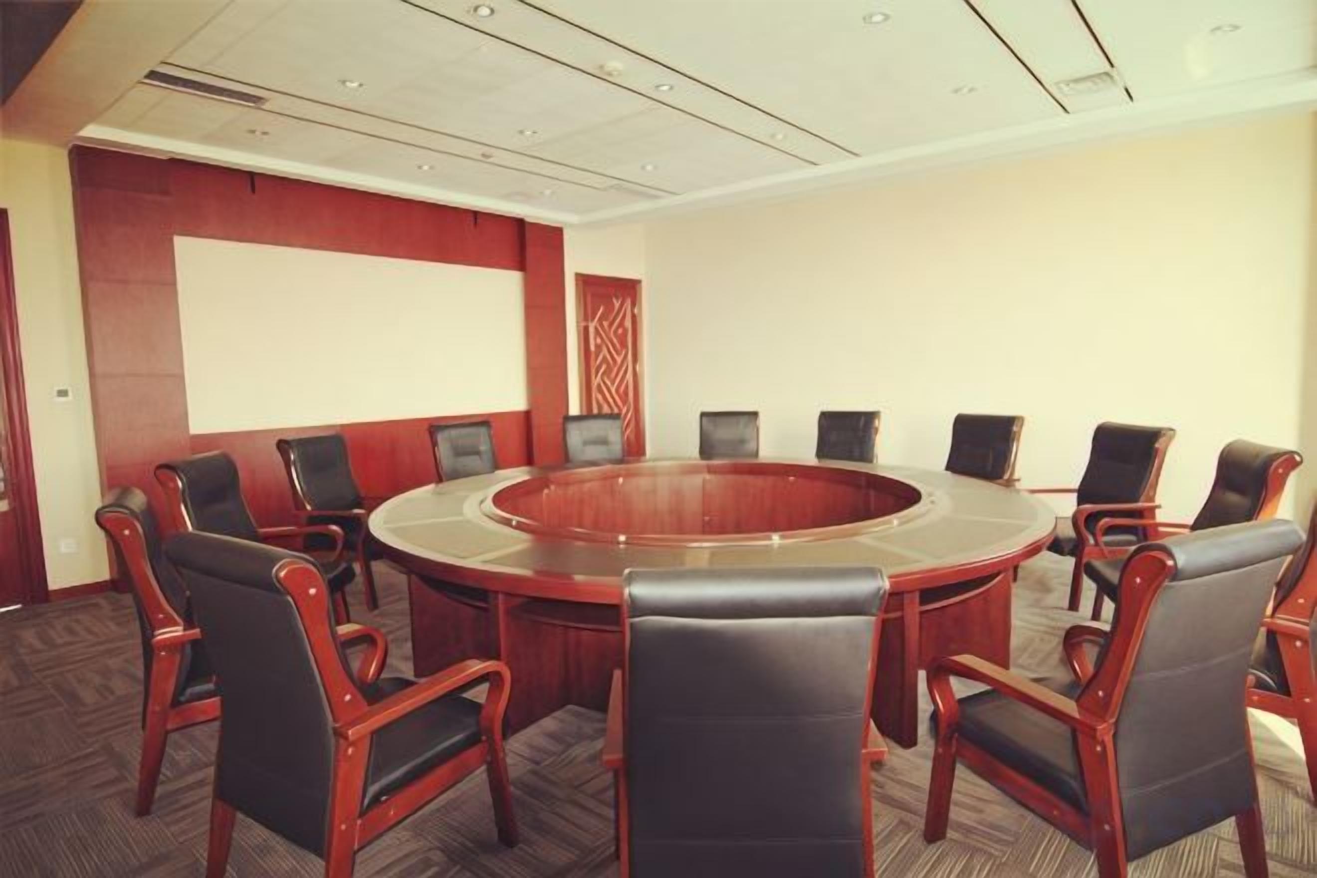 A conference room with a round table and chairs, a projector screen, and a carpeted floor.
