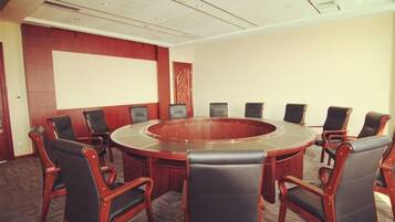 A conference room with a round table and chairs, a projector screen, and a carpeted floor.