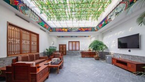 Sala de estar em estilo tradicional, com teto alto, televisão montada na parede e uma grande janela com treliça de madeira decorativa.