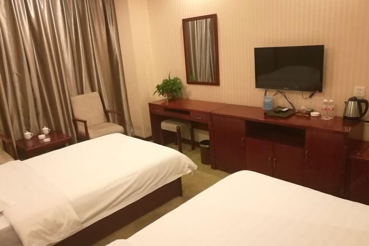 Une chambre d’hôtel avec deux lits, un bureau, une chaise, une télévision et une petite table sur laquelle se trouvent une plante et des articles de toilette.