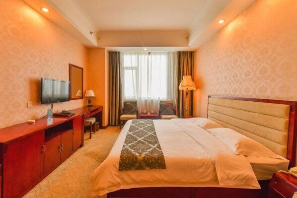 A hotel room with a bed, a desk, a television, and a window with curtains.