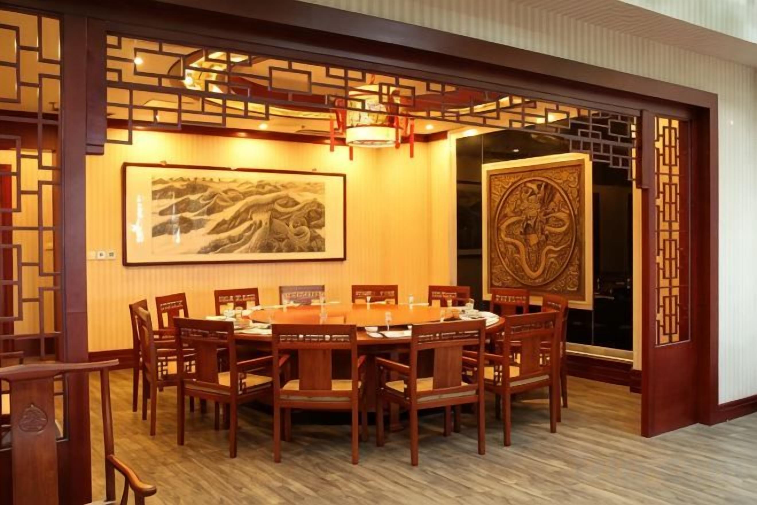 A traditional-style dining area with a round table and chairs, framed artwork on the walls, and a decorative wooden screen.