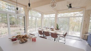 Une salle à manger spacieuse, avec une grande table dressée pour six personnes, entourée de grandes fenêtres donnant sur la forêt.