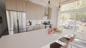 Une cuisine moderne dotée d’un grand îlot central, d’appareils électroménagers en acier inoxydable et offrant une vue sur l’extérieur.